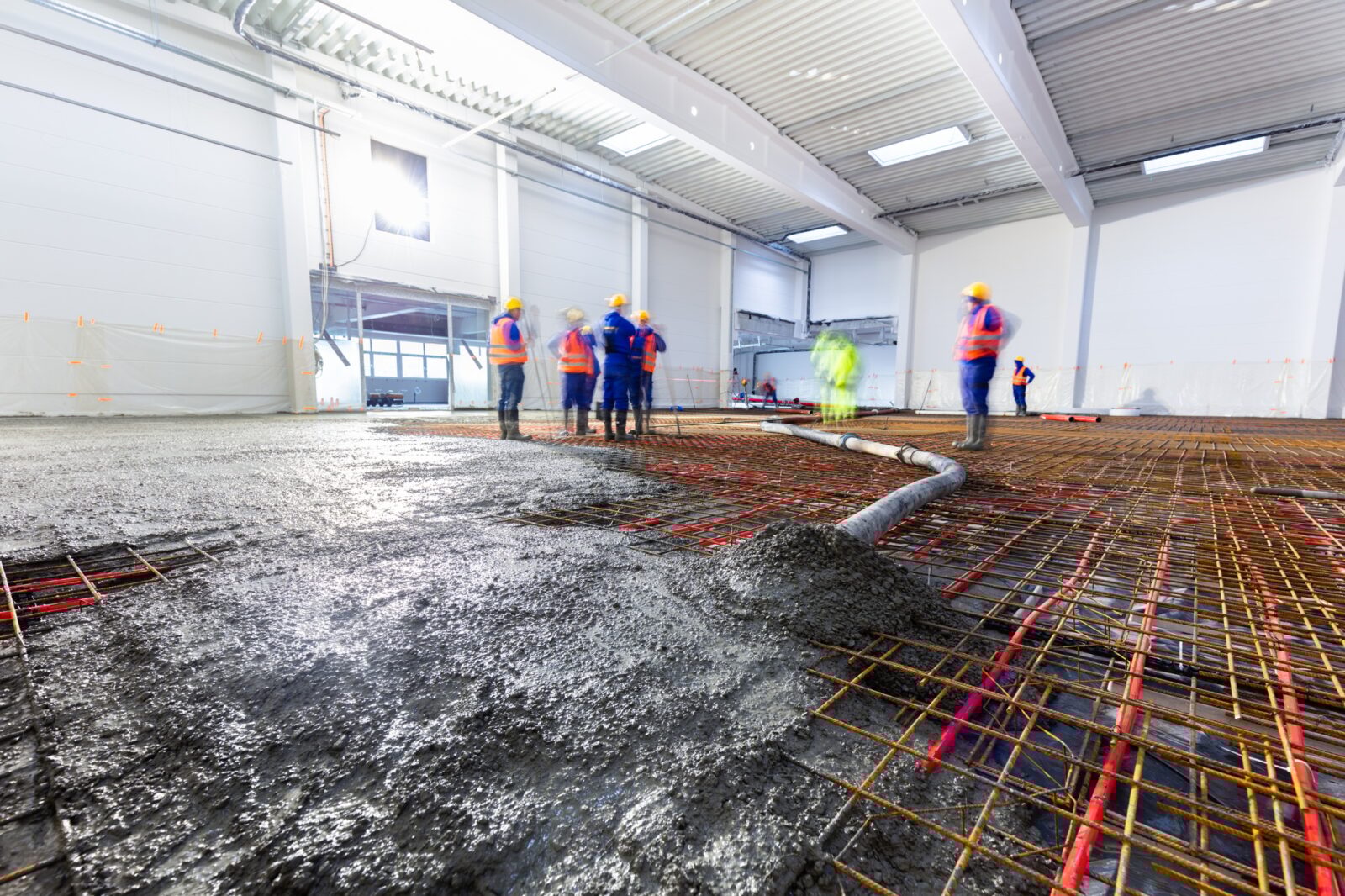 Workers do concrete screed on floor with heating in a new warehouse building